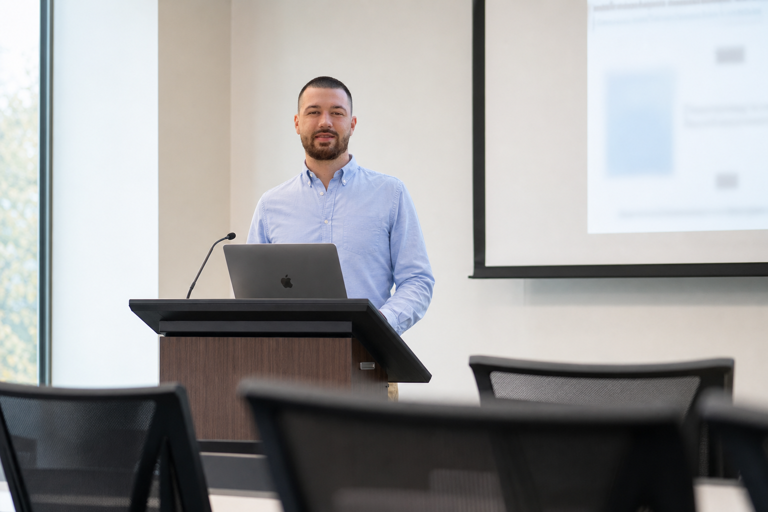 Chandler Drake Talley photo: teaching at a classroom lectern with a laptop Chandler Drake Talley, Senior AI Engineer — teaching at a classroom lectern with a laptop